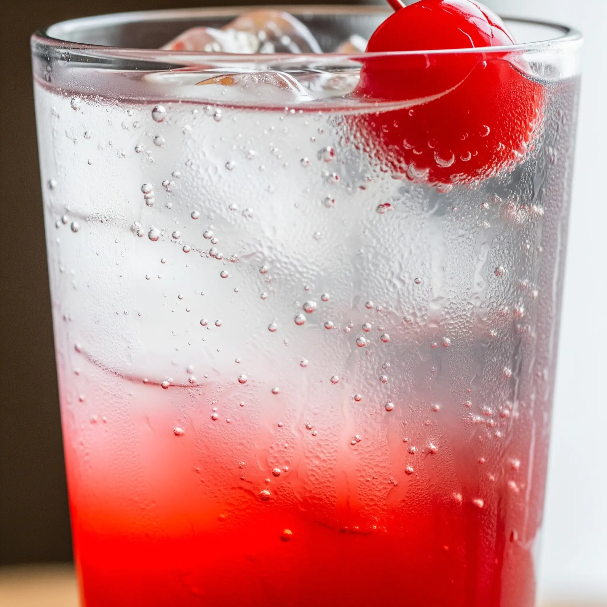 A close-up shot of a Shirley Temple in a tall glass, highlighting the red grenadine at the bottom, the clear ginger ale, and the maraschino cherry garnish.